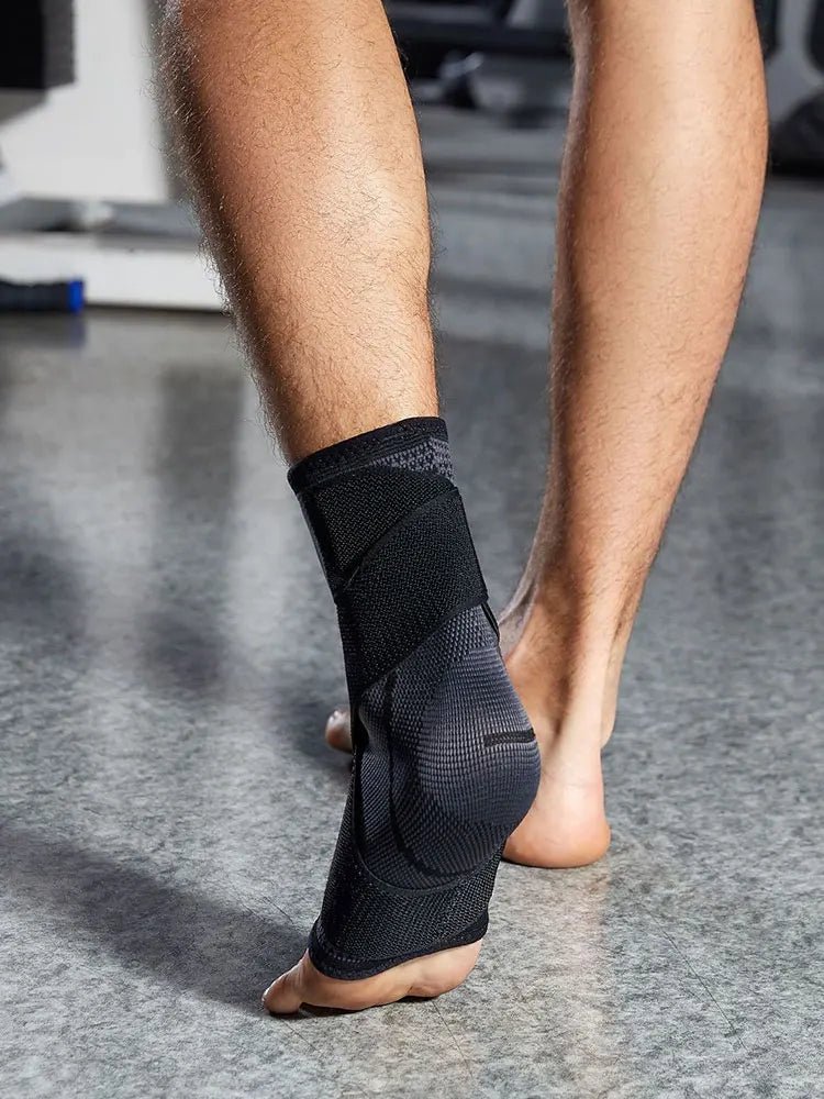 Die Rückansicht eines Fußes im Fitnessstudio zeigt die anatomische Passform der dunklen Knöchelbandage an der Ferse und Achillessehne. Die über Kreuz verlaufenden schwarzen Kompressionsriemen umschließen den Knöchelbereich fest, um maximale Stabilität bei sportlichen Bewegungen zu bieten.